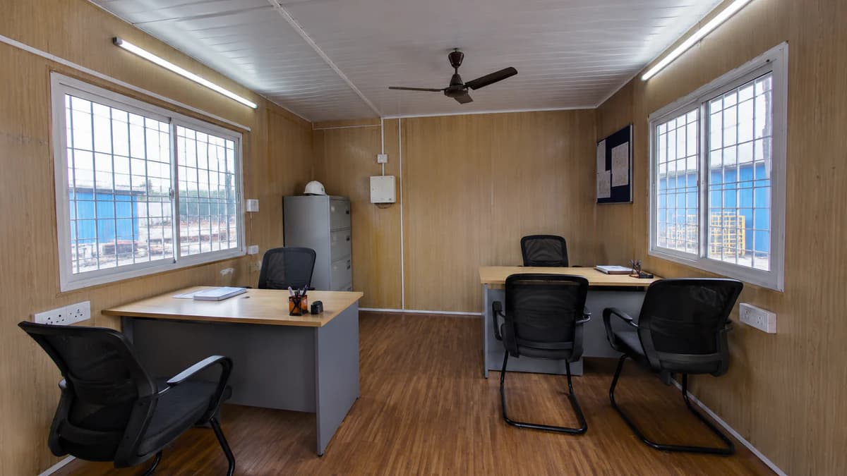 Portable cabin office interior with twin desks, office chairs, a filing cabinet and grilled sliding windows on wood walls