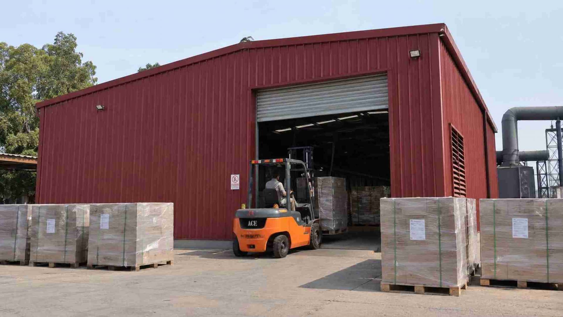 Forklift moving a pallet into a burgundy storage shed through a wide roller door.