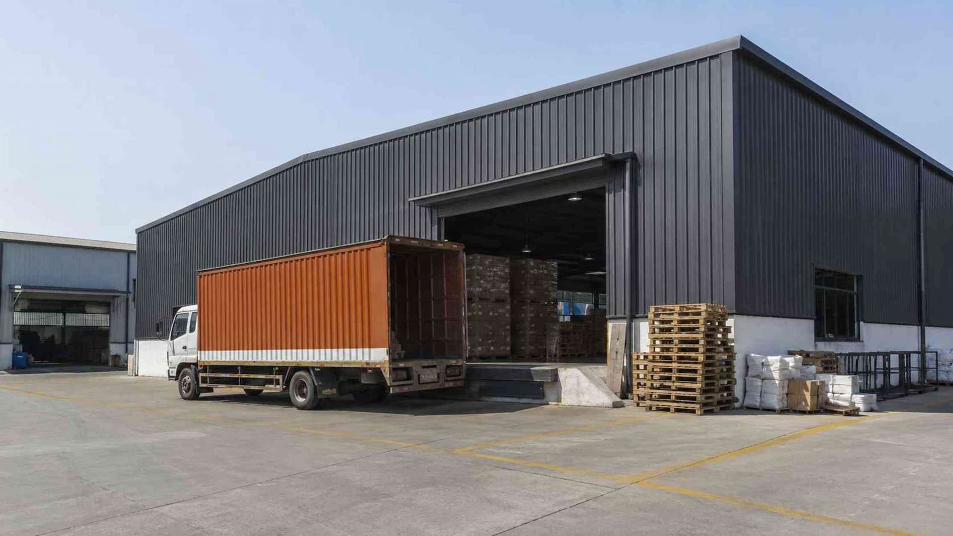 Charcoal storage shed at a logistics yard with a delivery truck reversed to the loading door.