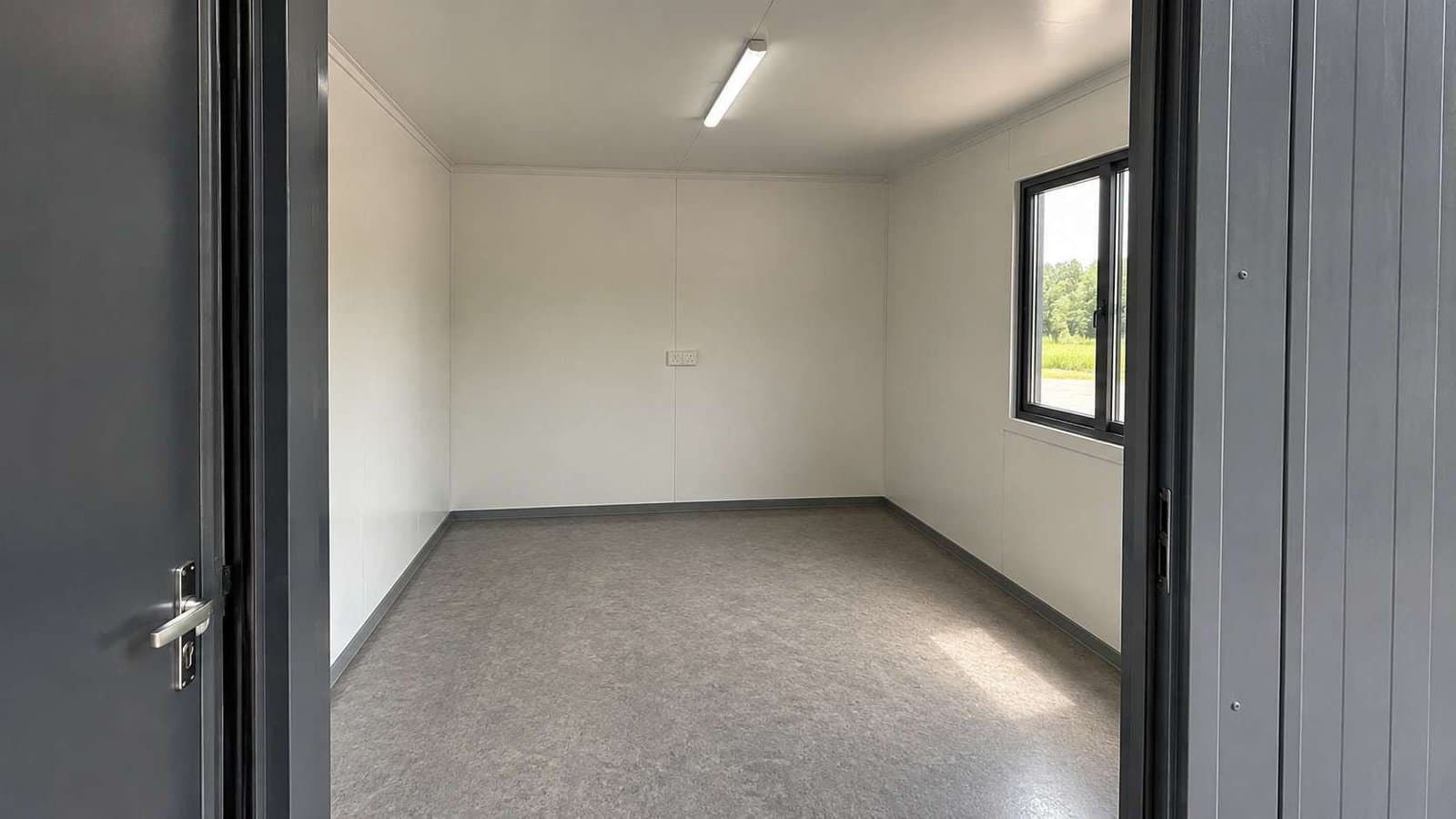 Inside a container building showing white MD-board lining, vinyl floor and wall switchboard.