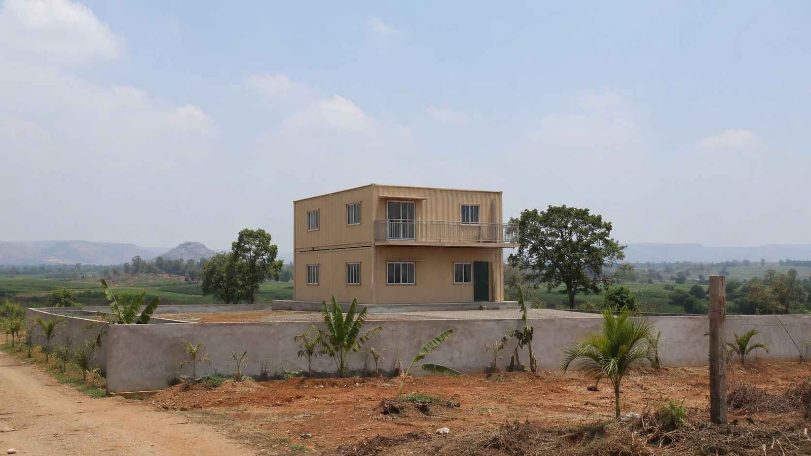 Two-storey Sandstone Beige container home placed on a rural farmland plot in mid-afternoon natural light.