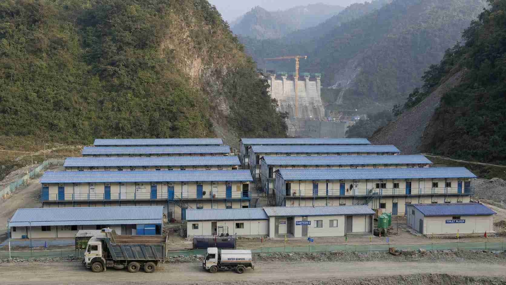 Large SAMAN labor accommodation camp on a hilly-terrain dam construction project site in India with multi-row dormitory blocks.