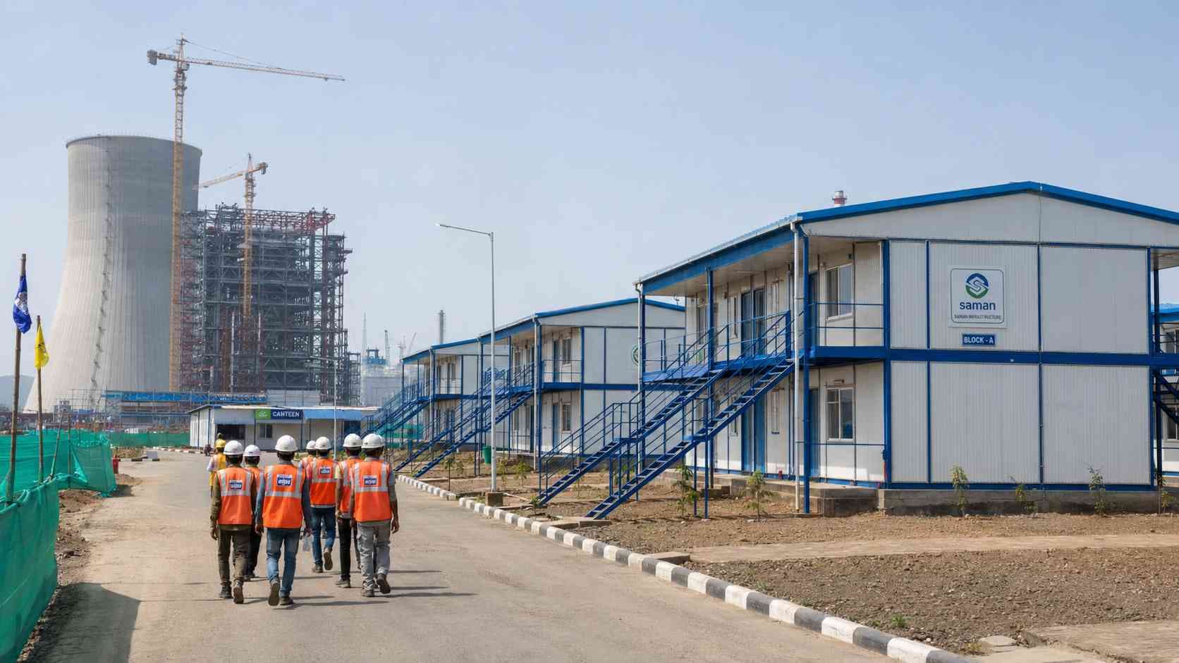 Labor accommodation cluster on the periphery of a thermal power plant construction site in India with cooling tower silhouette in the background.