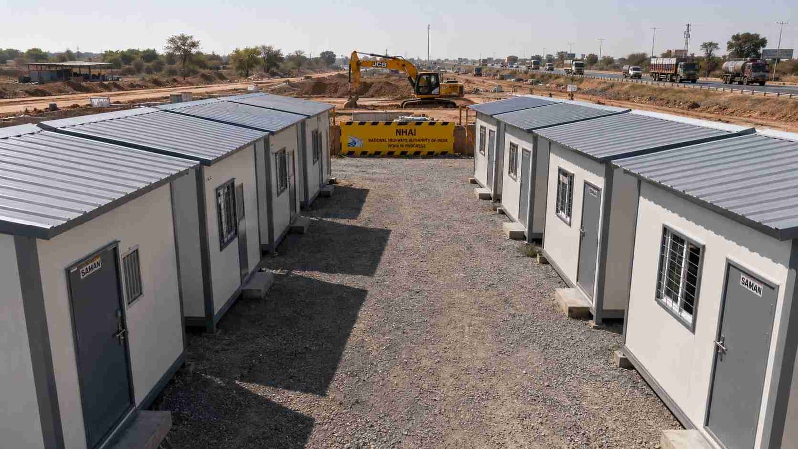 SAMAN labor hutment camp deployed beside a National Highway construction project with NHAI signage and earthworks plant visible.