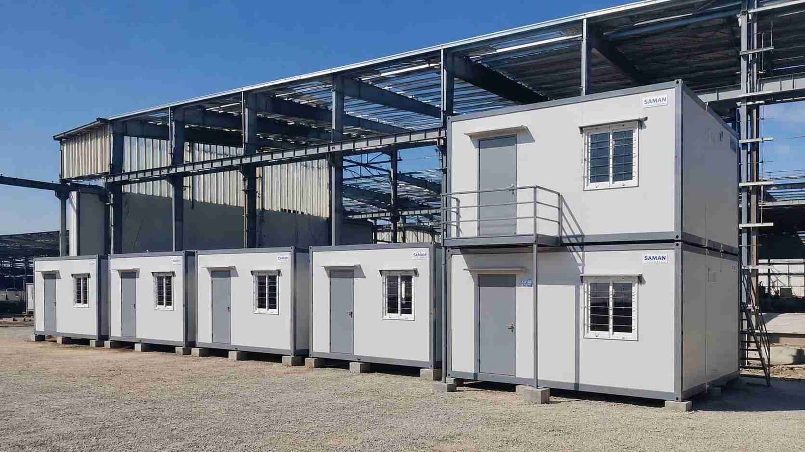 SAMAN labor hutment camp in Steel Grey beside a partially-clad pre-engineered factory building under construction.