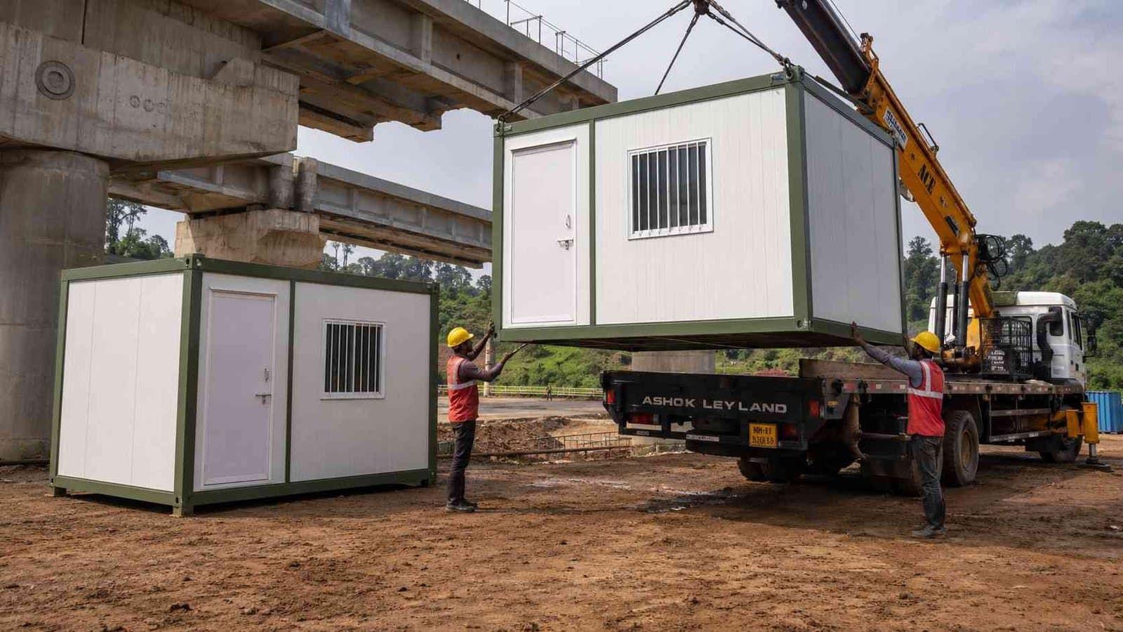 Sage Industrial prefab labor hutment being offloaded from a truck at an Indian bridge construction site by two workers.