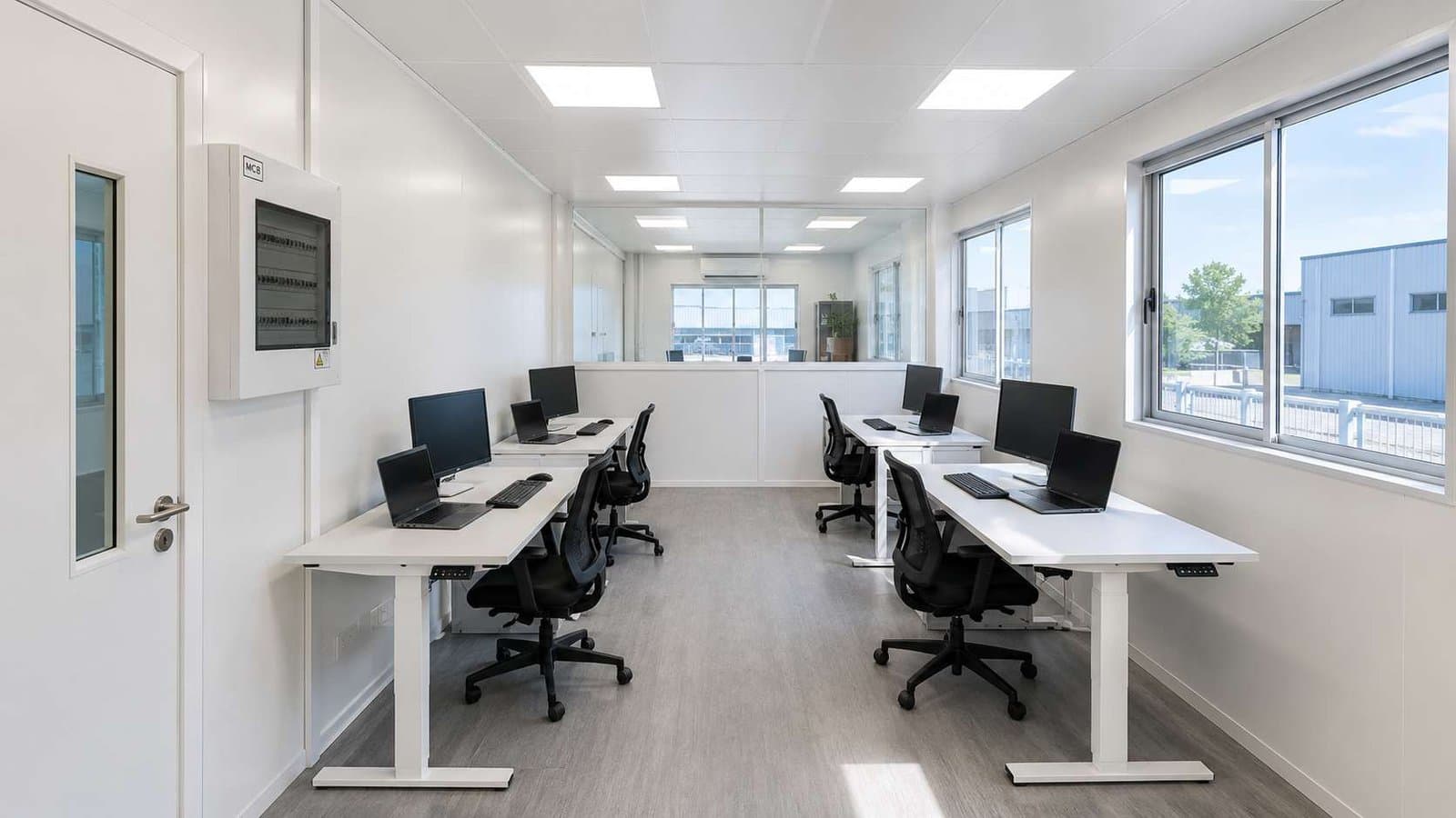 Ground floor workstation area inside white modular portable office with six desks, partition wall, and LED ceiling