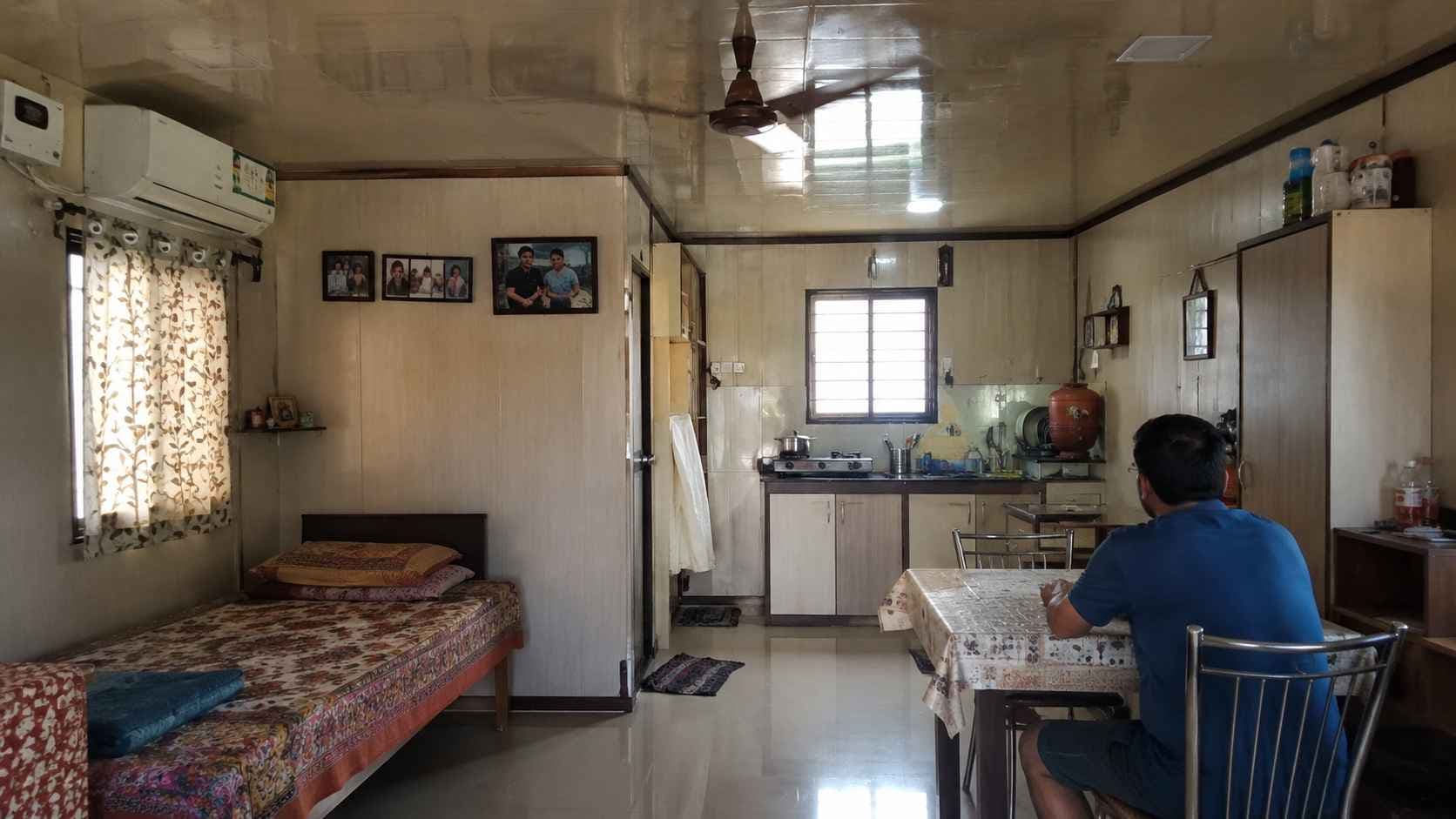 Interior of a porta cabin house lived in as a home, with bed, kitchen and an AC unit.