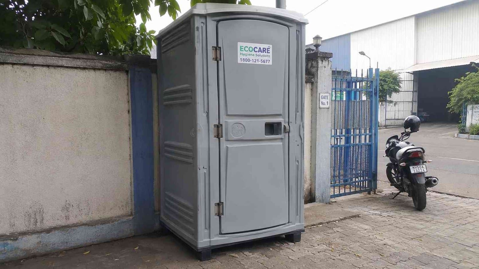 Pearl grey portable toilet cabin installed near a factory gate in an industrial area