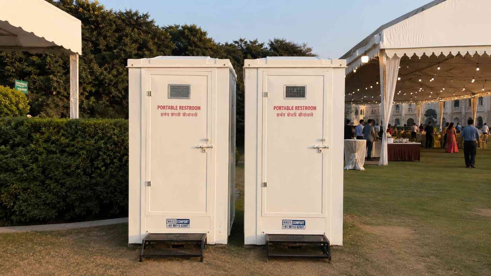 Two white portable toilet cabins set up on grass at an outdoor event venue