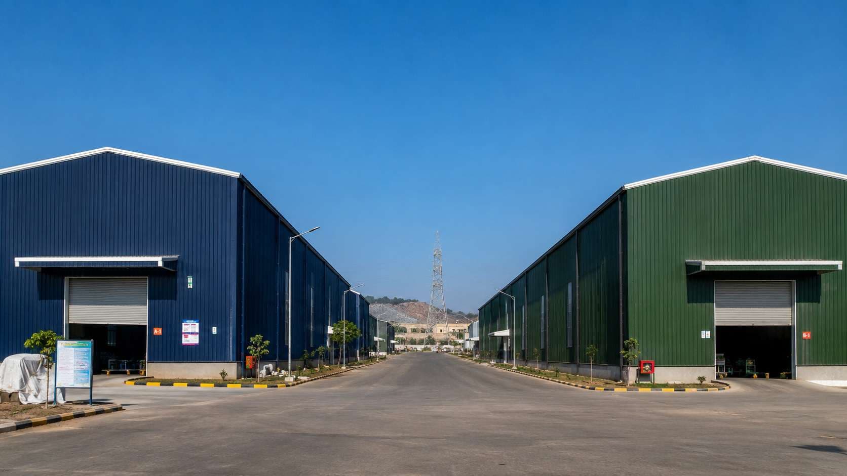 Two identical large pre-engineered buildings, one navy and one green, side by side at an Indian industrial zone.