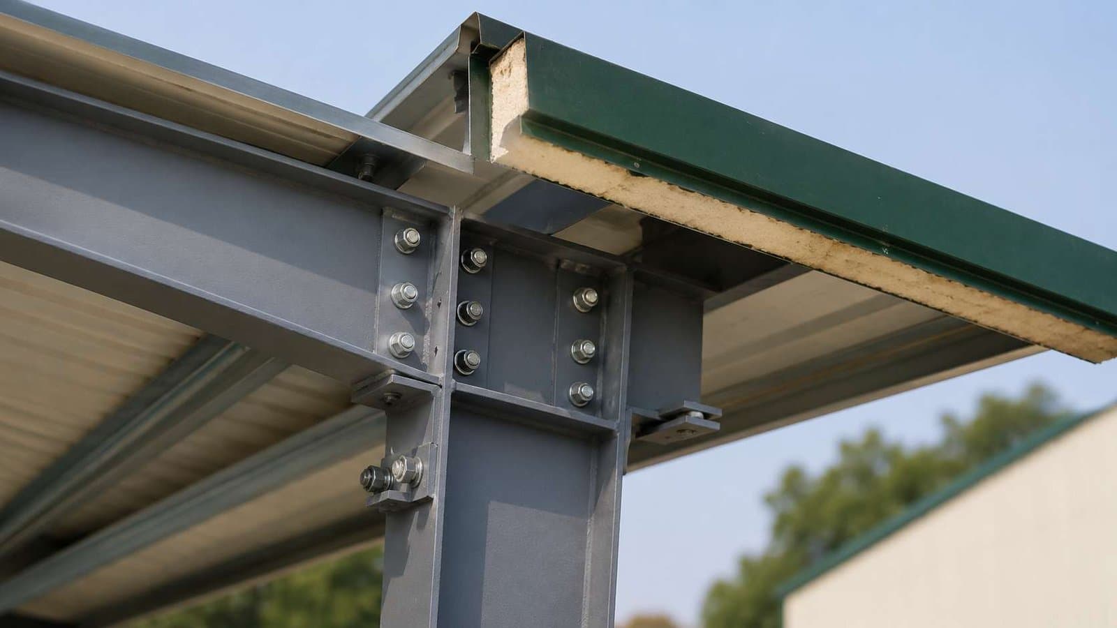Close detail of a steel column, rafter and green PUF panel edge showing the insulation core.