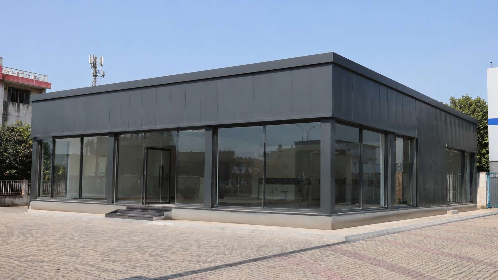 Charcoal prefab commercial building full elevation on a paved commercial plot, three-quarter daylight view.