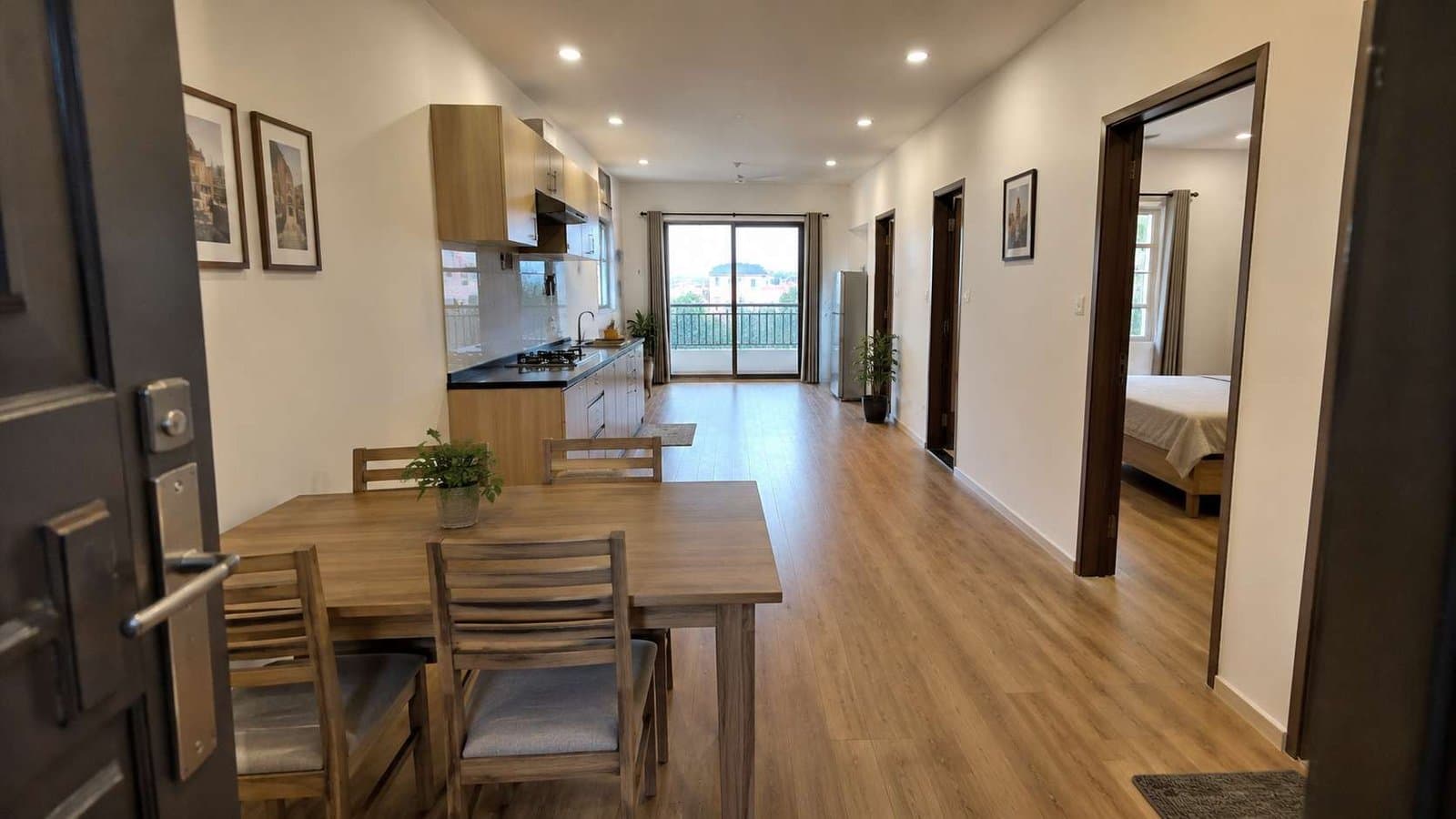 Through-the-door interior view of SAMAN prefab container home showing dining area, kitchen, bedroom doorway, and balcony slider in one frame.