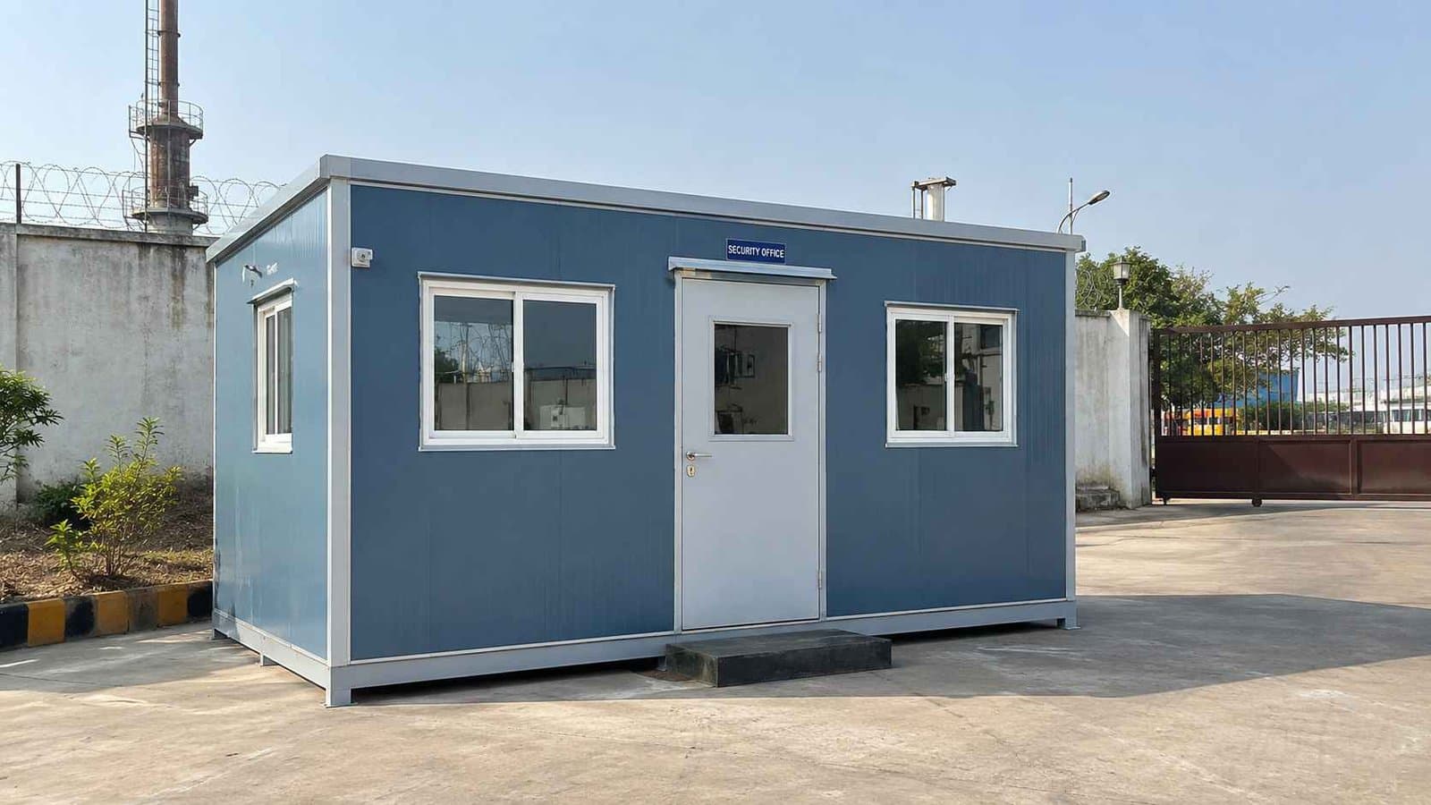 Steel blue prefab office building at a factory compound entrance serving as the admin office