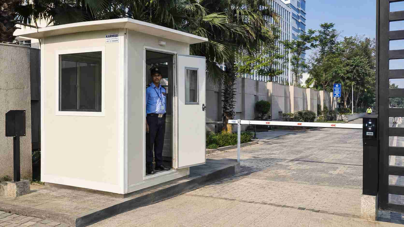 Prefabricated security cabin installed at a corporate-compound entrance gate in India, off-white factory finish.