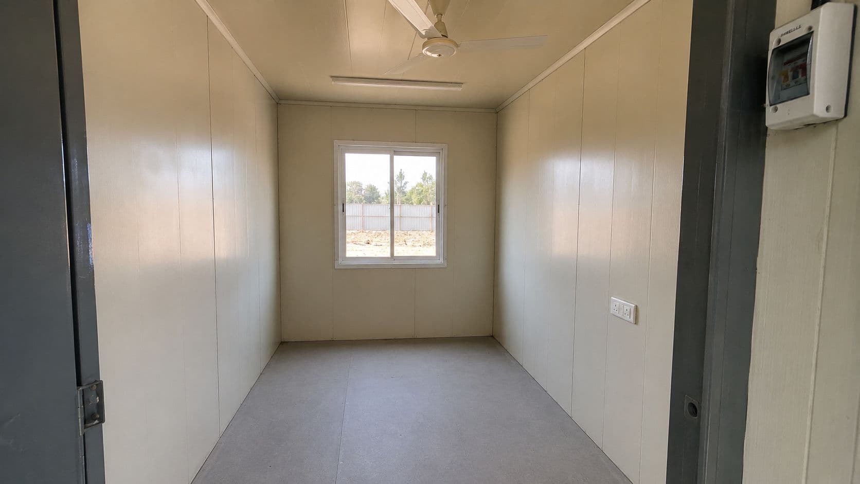 Interior of an 8'×6' readymade security cabin showing the standard electrical fitout — one ceiling light, one fan point, one wall socket