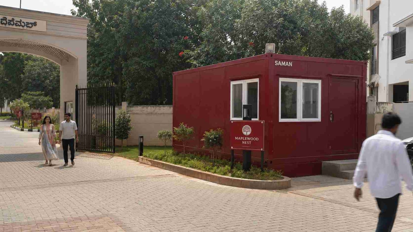 Burgundy red SAMAN prefab office at a gated residential layout entrance with paver driveway.