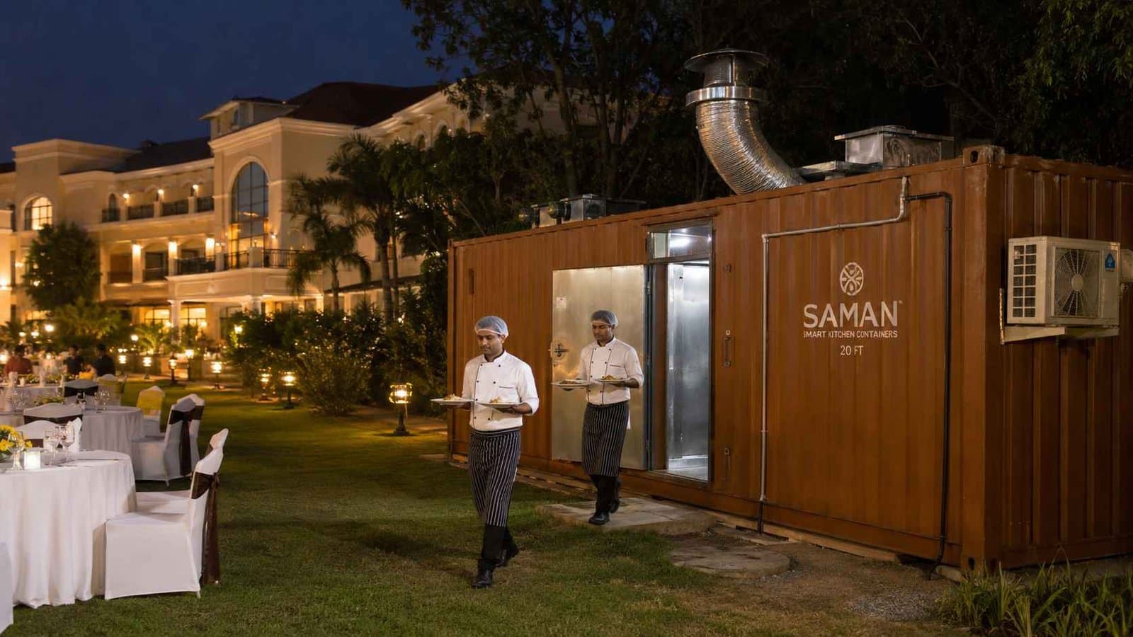 Hotel F&B kitchen container running behind a Hosur resort property's lawn-dining venue with service staff carrying plated food to the dining area