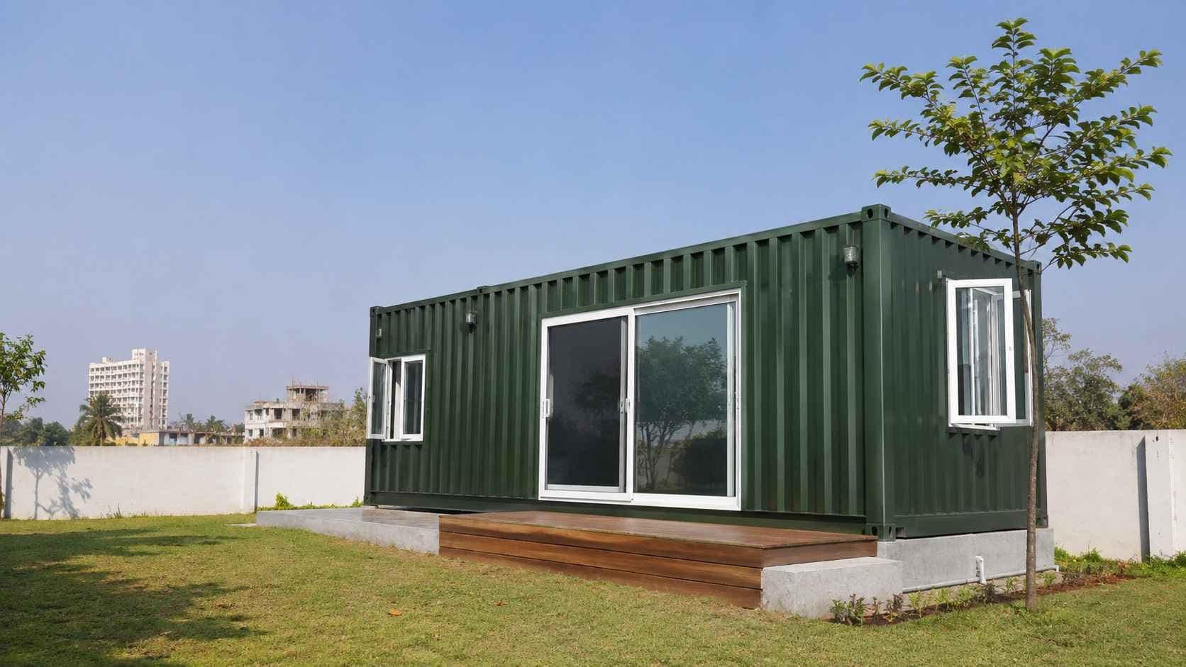 Forest green storage container house on a suburban Bengaluru plot with a wooden deck step and side windows.