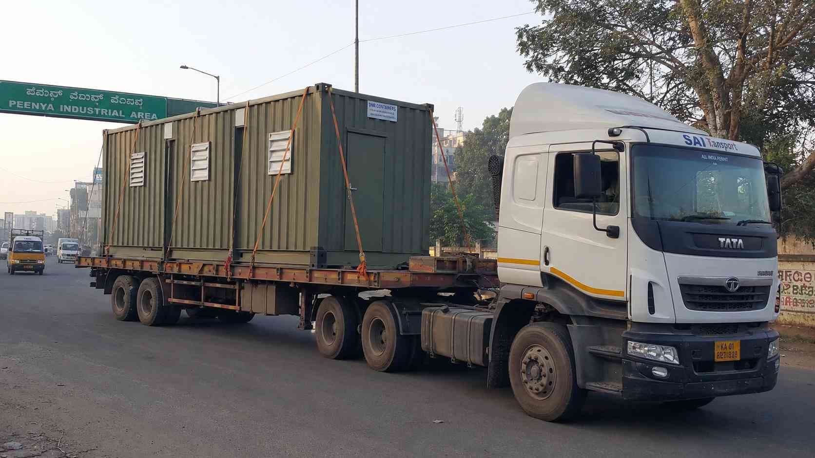 Porta cabin in Sage Industrial green being delivered on a low-bed trailer along Tumkur Road into Peenya during the early-morning dispatch window.