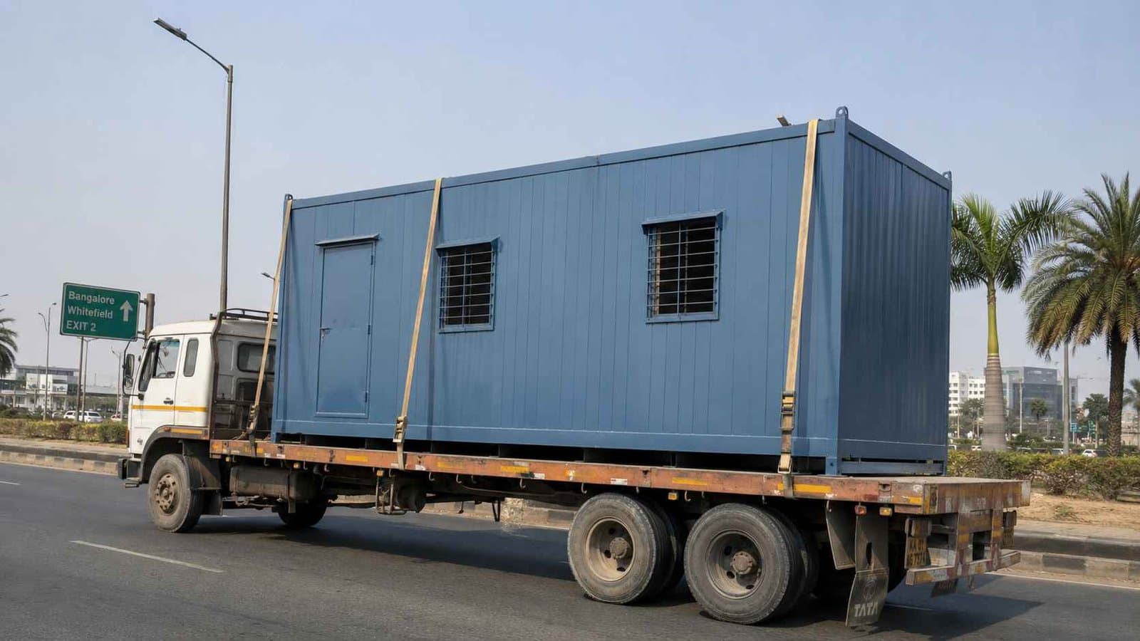 Steel Blue porta cabin loaded single-piece on a flatbed truck approaching Whitefield via Bangalore ORR.