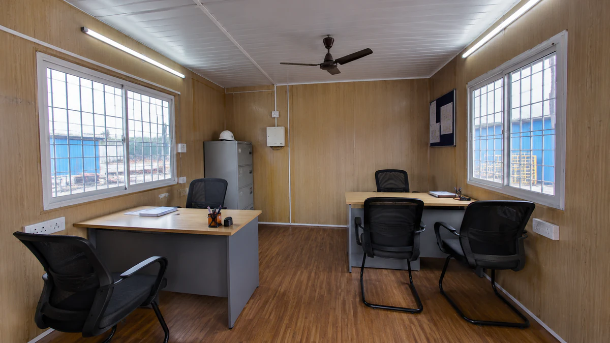Portable cabin office interior with twin desks, office chairs, a filing cabinet and grilled sliding windows on wood walls