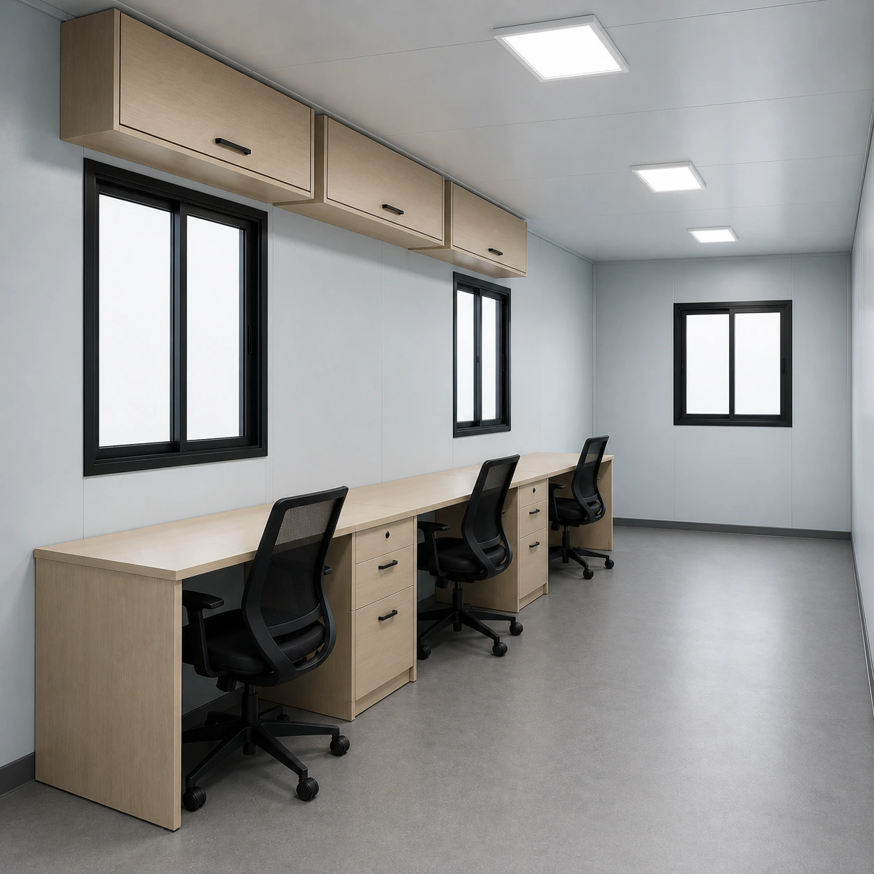 Three desks, three mesh chairs and three wall-fixed cabinets along one long wall below two sliding windows