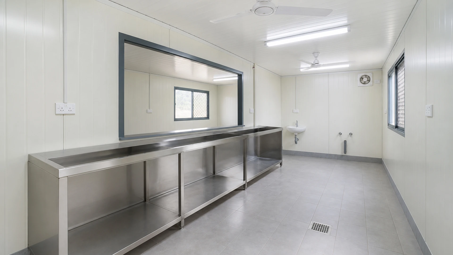 Empty stainless counter shell, hand-wash point and floor drain in a canteen service zone