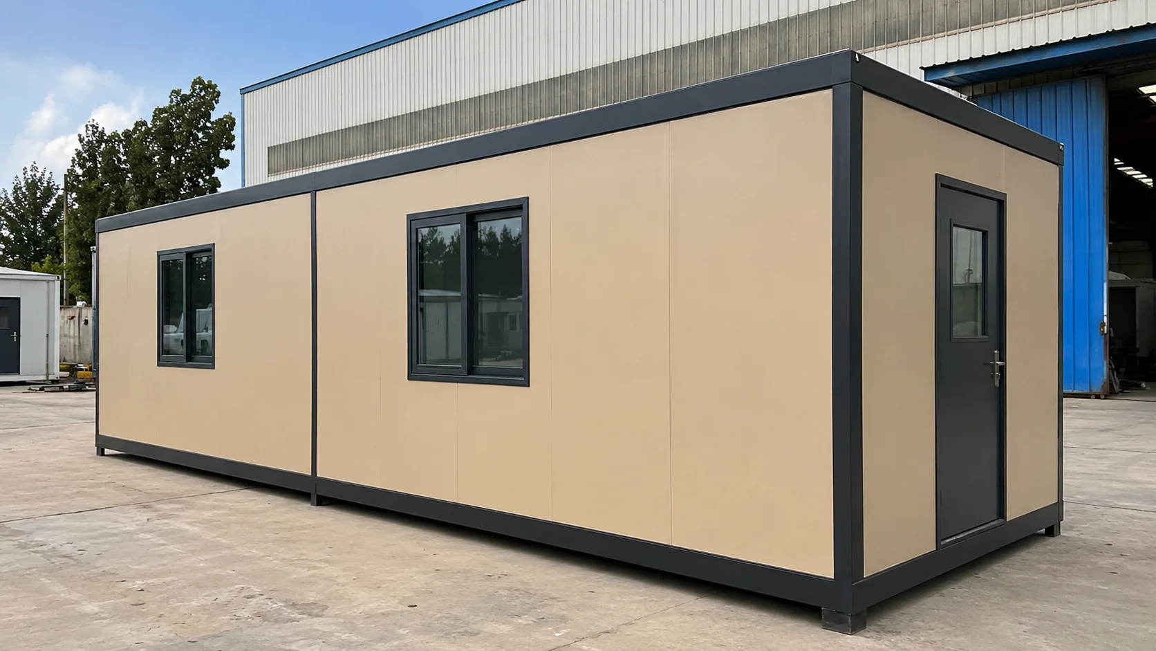 Beige PUF panel cabin in a factory yard with a glazed end door and a visible module junction seam