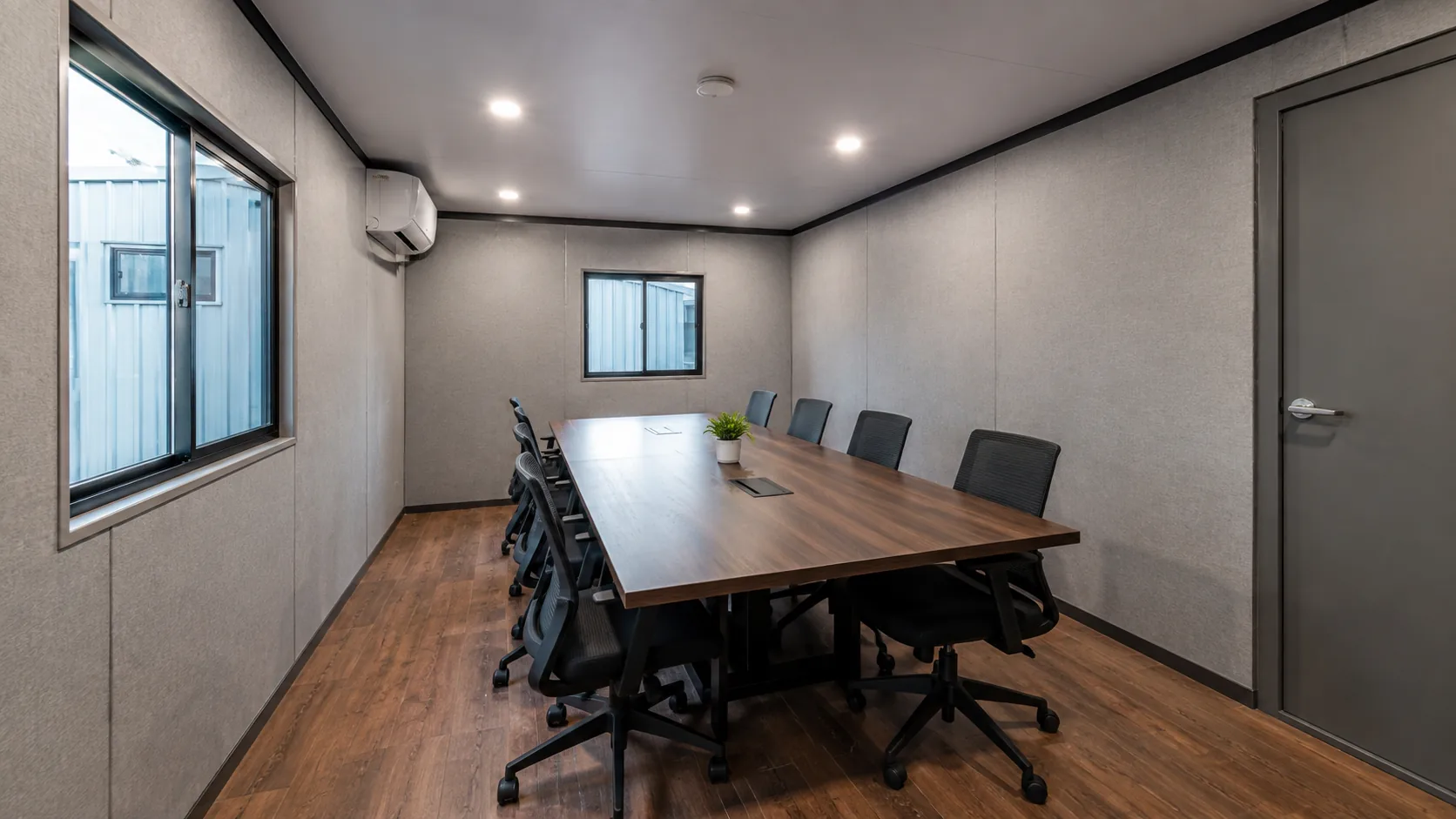 Cabin interior laid out as a meeting room, with a long table, eight chairs and a wall air conditioner